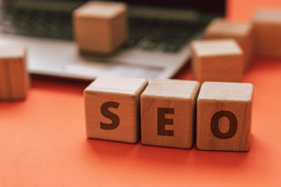Wooden blocks spelling SEO beside a laptop.